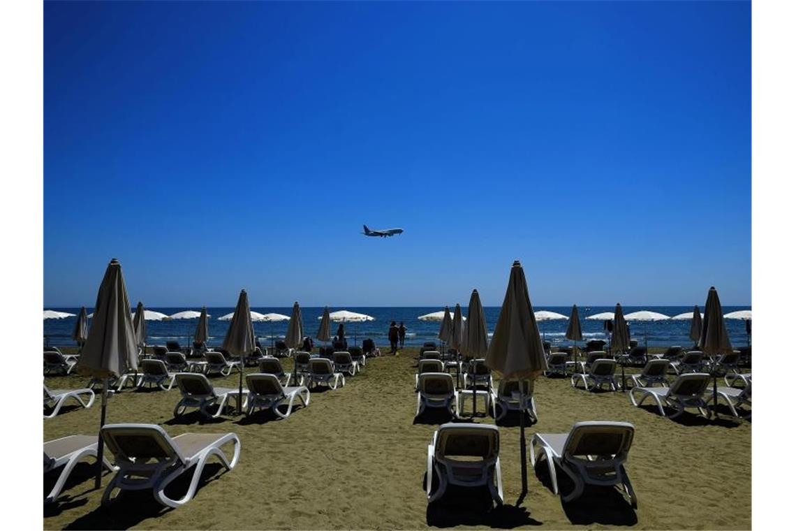 Einige Menschen sonnen sich am Makenzi Strand während sich im Hintergrund ein Flugzeug auf die Landung am internationalen Flughafen Larnaca vorbereitet. Zypern ist nun auch als Risikogebiet eingestuft. Foto: Petros Karadjias/AP/dpa