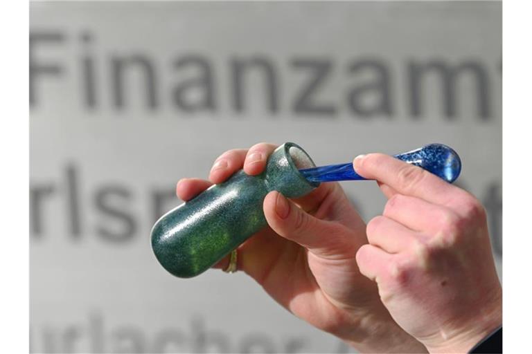 Ein Mann hält vor dem Karlsruher Finanzamt einen Flakon mit Banknoten-Duft, das Parfüm „Aerarium“, in der Hand. Foto: Uli Deck/dpa/Archivbild
