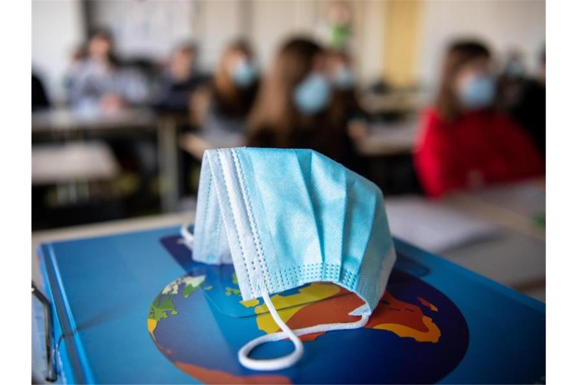Ein Mund-Nasen-Schutz liegt während des Unterrichts auf einem Atlas. Foto: Matthias Balk/dpa/Illustration