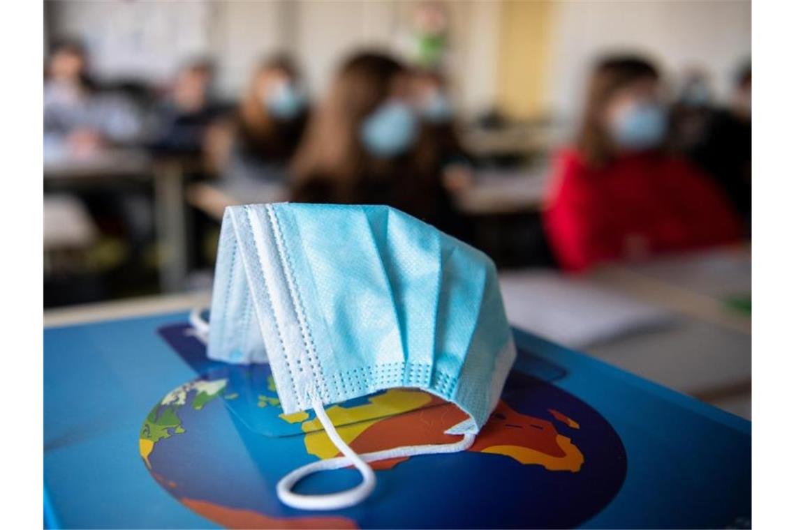 Lehramtsstudierende sollen Schülern helfen Ein Mund-Nasen-Schutz liegt während des Unterrichts auf einem Atlas. Foto: Matthias Balk/dpa/Illustration