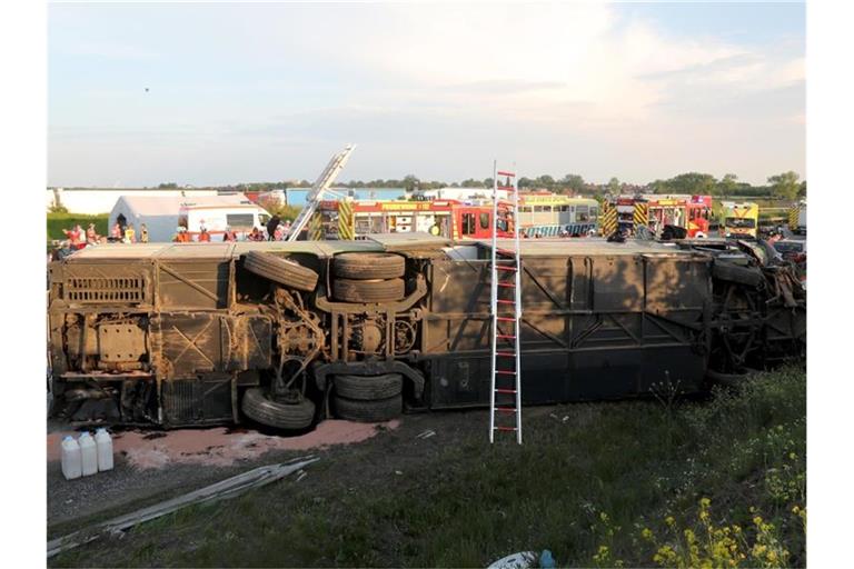 Einsatzkräfte der Feuerwehr stehen an der Unfallstelle neben dem verunglückten Bus. Der Bus überschlug sich zwischen den Anschlussstellen Leipzig-West und Bad Dürrenberg. Anschließend blieb das Fahrzeug auf der Seite liegen. Foto: Jan Woitas