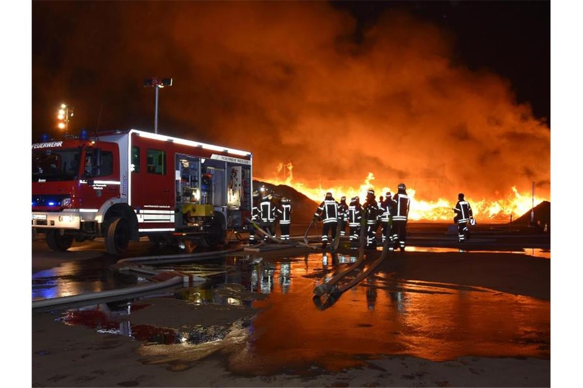 Einsatzkräfte der Feuerwehr stehen auf einem Wertstoffhof vor einem brennenden Komposthaufen. Foto: Julian Buchner/Einsatz-Report24