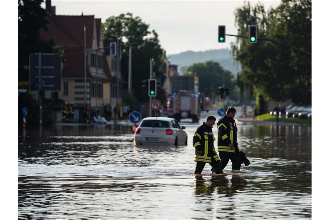 Einsatzkräfte der Feuerwehr waten über eine überschwemmte Kreuzung Ansbach. Foto: Nicolas Armer/dpa