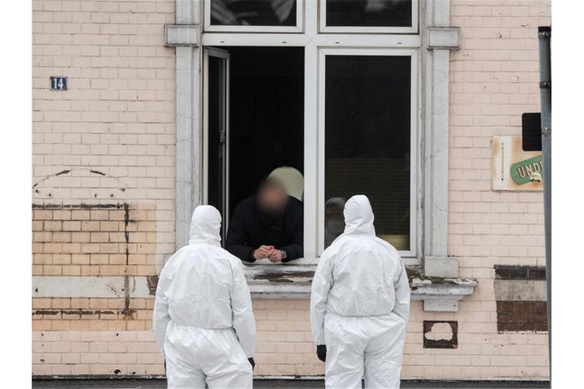 Einsatzkräfte der Polizei unterhalten sich durch ein Fenster mit einem Mann. Nach Angaben der Stadt war ein Bauarbeiter auf Montage positiv auf die Variante B.1.1.7 getestet worden. Foto: Bernd Thissen/dpa