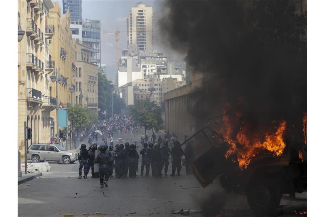 Einsatzkräfte stehen hinter einem brennenden Auto. Foto: Hassan Ammar/AP/dpa