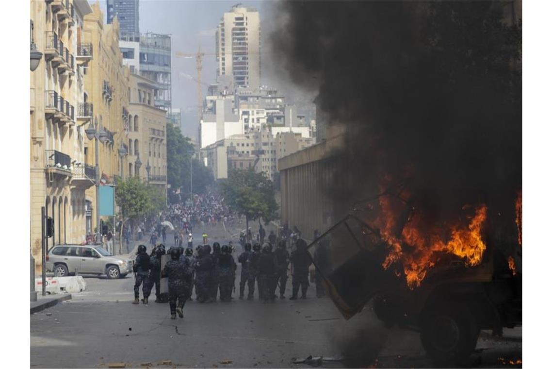 Beirut: Gewalt bei Protesten - Premier schlägt Neuwahlen vor Einsatzkräfte stehen hinter einem brennenden Auto. Foto: Hassan Ammar/AP/dpa