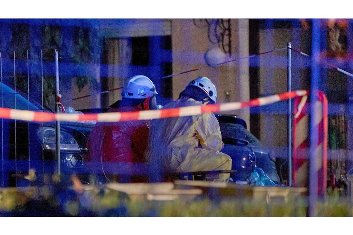 Einsatztkräfte in Schutzanzügen und mit Gasmasken sitzen im hessichen Runkel hinter einer Absperrung.