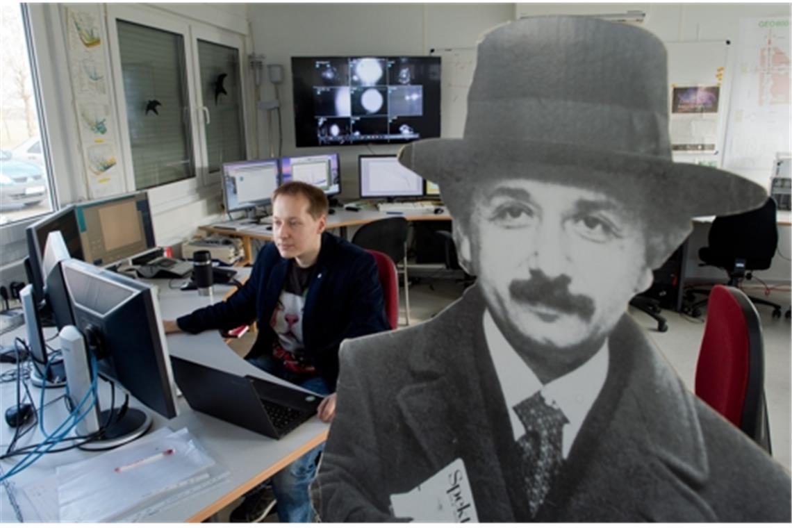 Einstein ist überall: Ein Wissenschaftler  sitzt in einem Kontrollraum des Gravitationswellendetektors GEO600 neben einem Pappaufsteller, der Albert Einstein, den deutschen Physik-Nobelpreisträger von 1922,  darstellt.