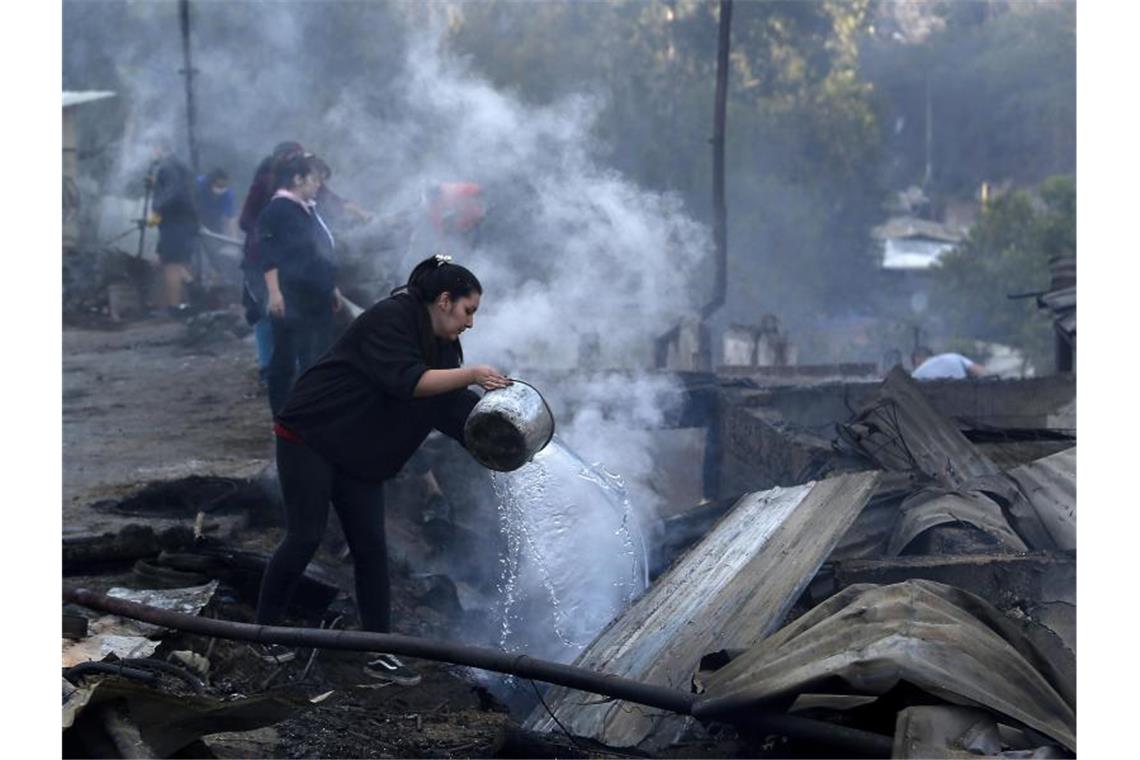 Mindestens 150 Häuser bei Bränden in Chile beschädigt Einwohner schütten Wasser auf die qualmenden Überreste ihrer Häuser, die bei einem Brand zerstört wurden. Foto: Raul Zamora/Aton Chile/dpa
