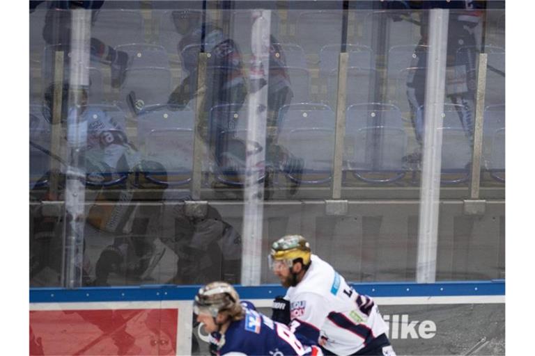 Eishockeyspieler spiegeln sich vor leeren Rängen in der Bande. Foto: Bernd Thissen/dpa/Symbolbild