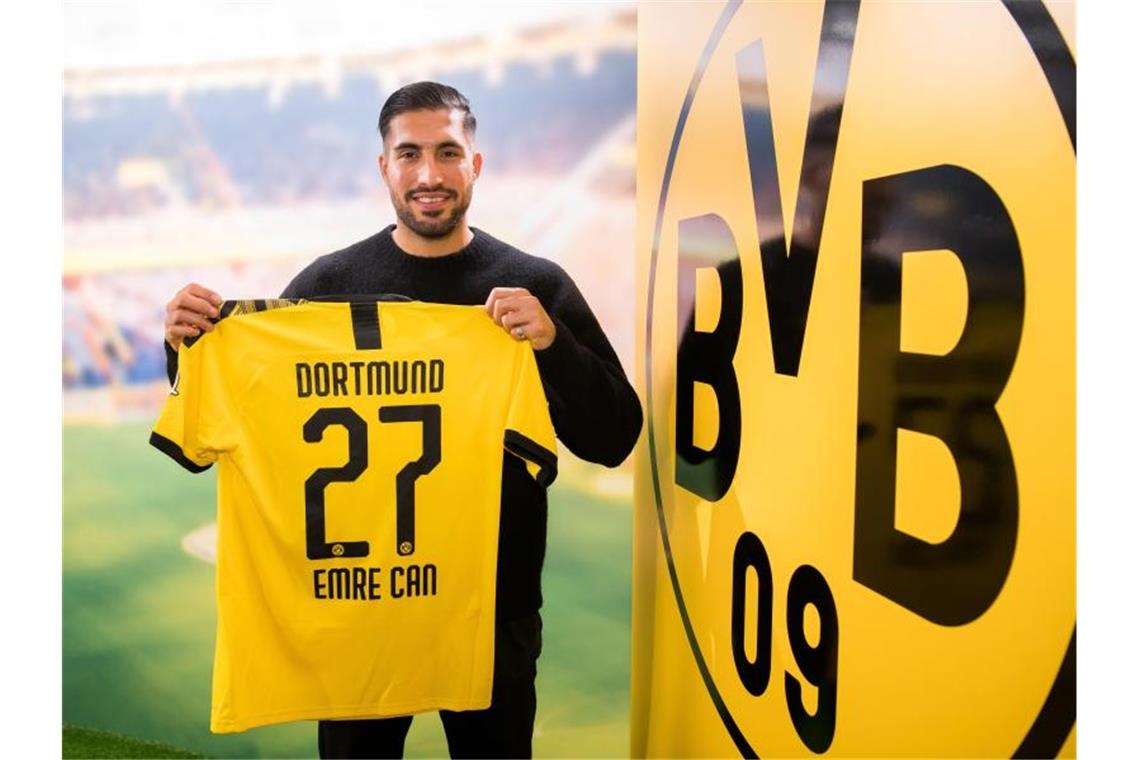 Nächster BVB-Coup: Emre Can kommt von Juventus Turin Emre Can posiert neben dem Logo von Borussia Dortmund mit einem Trikot des Vereins. Foto: -/BVB/dpa
