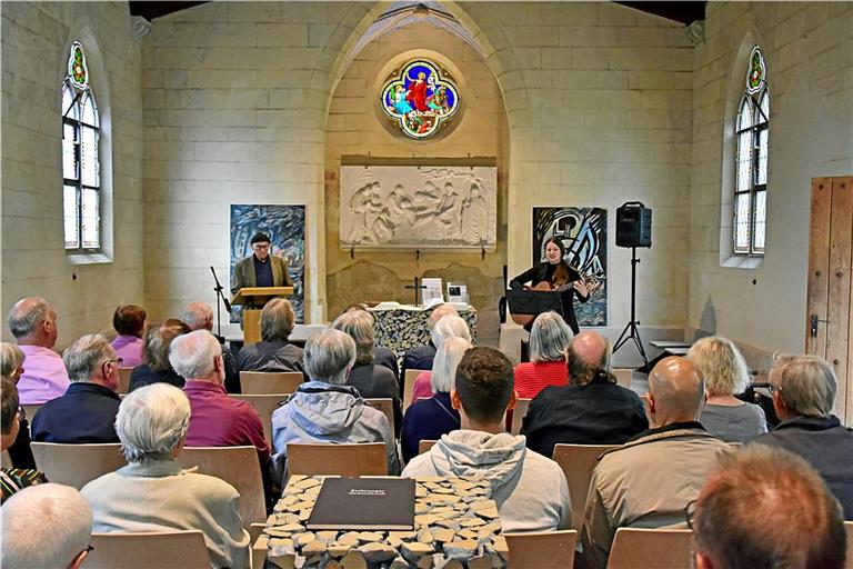 Ernst Hövelborn spricht beim Antikriegstag in der Friedhofkapelle über den Friedenspfarrer Otto Umfrid. Pia Sophie Stahl spielt zum Einklang das Lied „Lieg ich einst im Massengrab“. Im Hintergrund: zwei Gemälde von Ernst und Clemens Hövelborn. Foto: Tobias Sellmaier