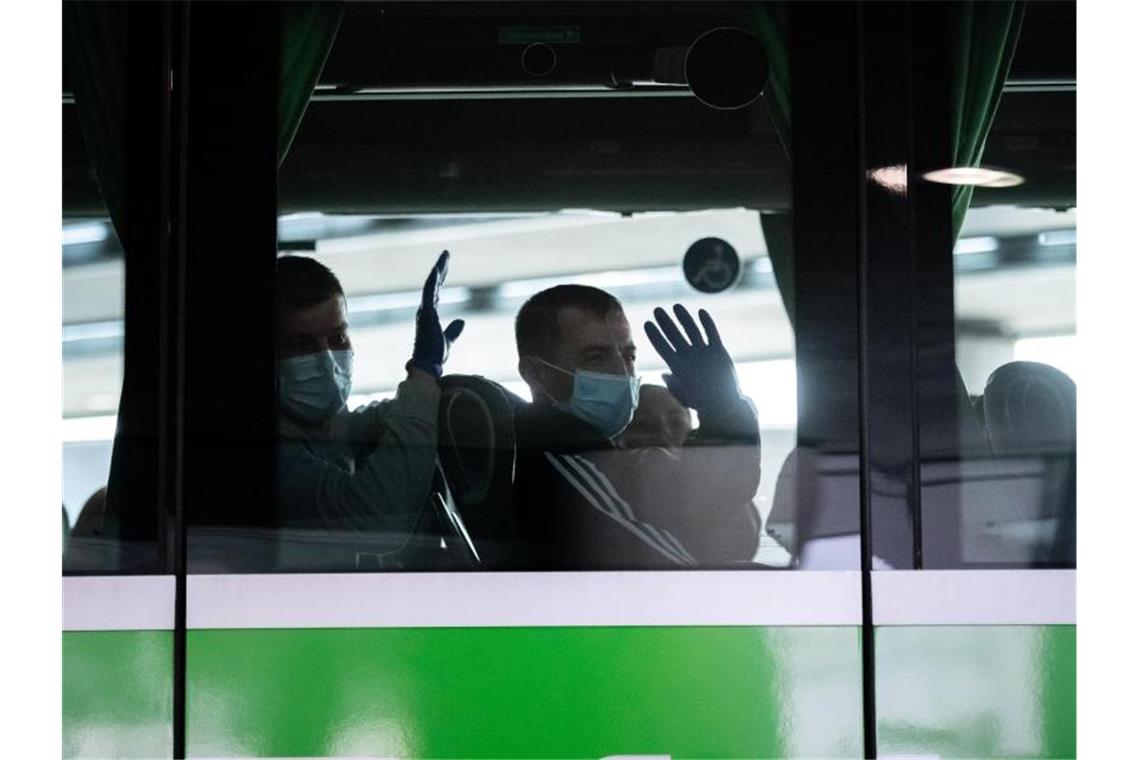 Erntehelfer sitzen mit Mundschutz in einem Bus am Terminal und winken zur Begrüßung. Foto: Fabian Strauch/dpa/Archivbild