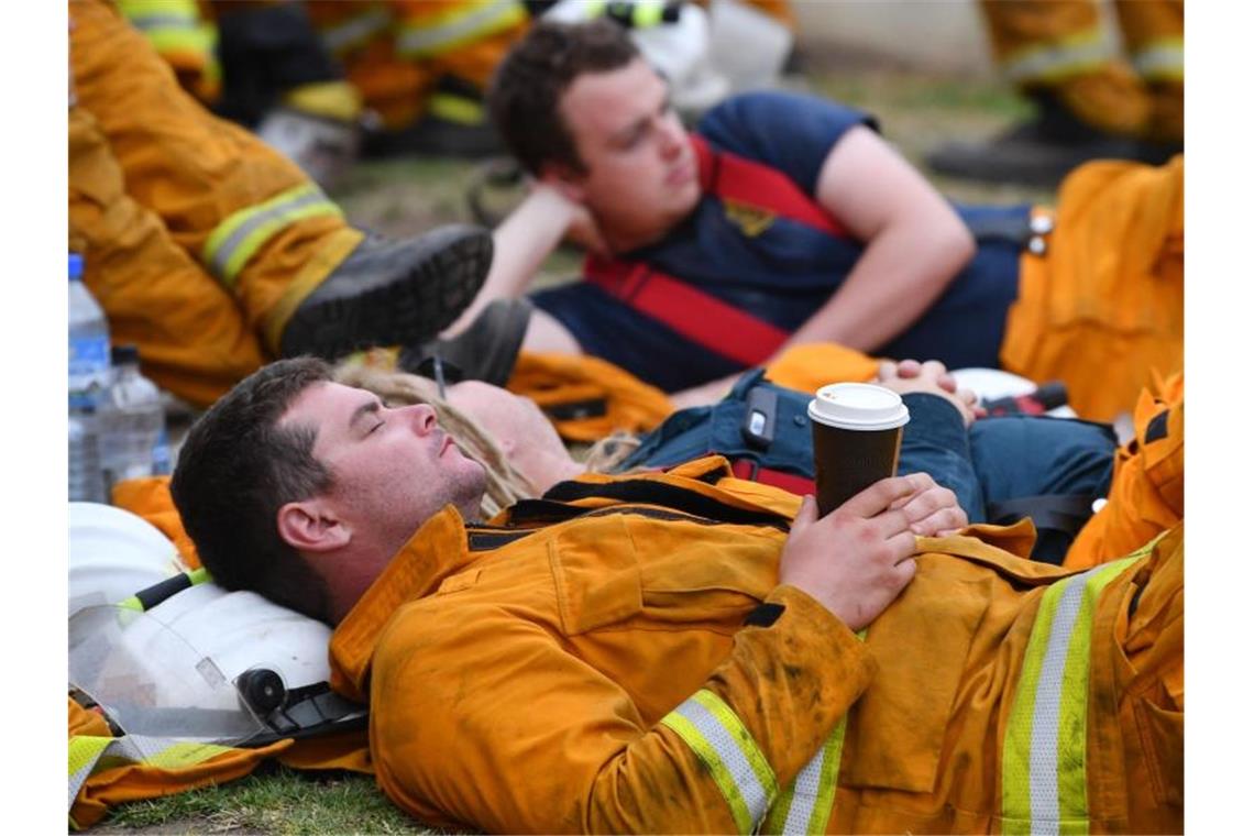 Erschöpfte Feuerwehrleute ruhen sich während eines Einsatzes gegen Buschbrände bei Adelaide aus. Foto: David Mariuz/AAP/dpa
