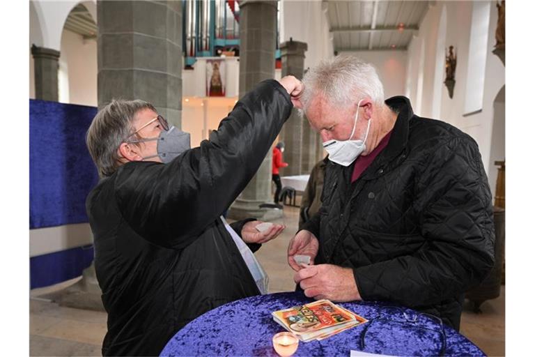 Evi Gräble-Kopp macht ihrem Mann Franz Kopp in der Pfarrkirche Sankt Jodok mit Asche ein Kreuz auf die Stirn. Foto: Felix Kästle/dpa