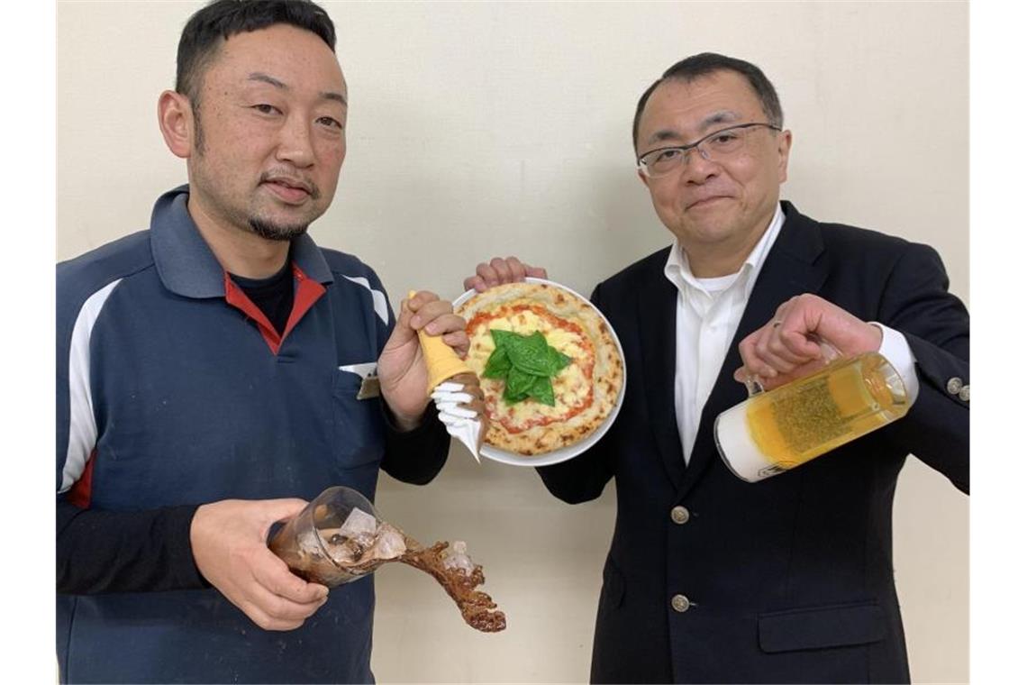 Künstlich wie köstlich: Japans hohe Kochkunst als Attrappe Fabrikleiter Hiroaki Miyazawa (l.) und Firmensprecher Yuta Kurokawa mit Repliken: eine Pizza, eine Maß Bier, eine Cola mit Eiswürfeln während des Einschüttens und ein Softeis. Foto: Lars Nicolaysen/dpa