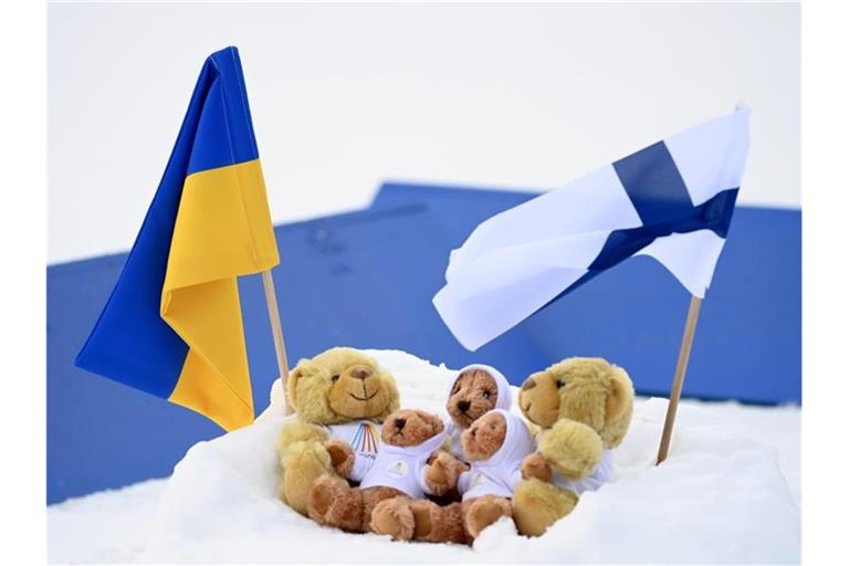 Fahnen der Ukraine und Finnlands in Kontiolahti neben den Weltcup-Maskottchen im Schnee. Foto: Vesa Moilanen/Lehtikuva/dpa