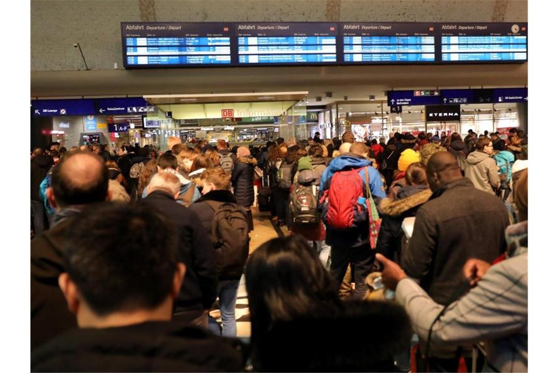 Fahrgäste der Bahn stehen vor der Informationsanzeige. Foto: Oliver Berg/dpa