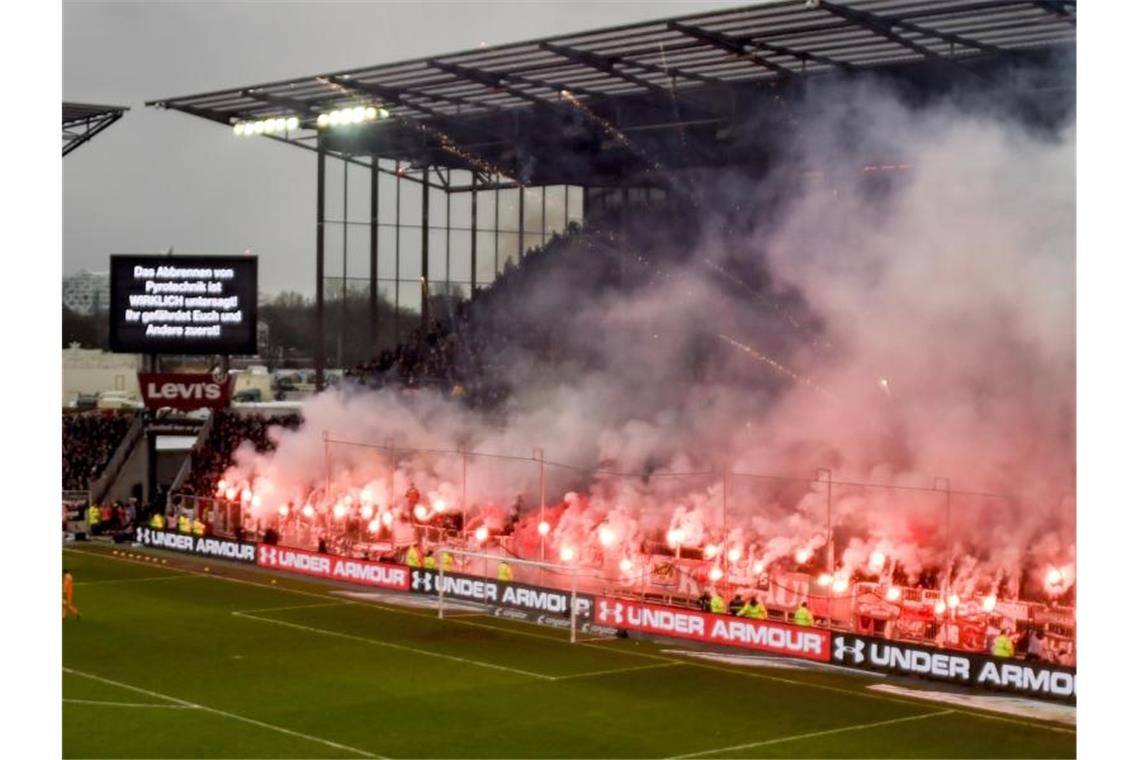 Fans brennen beim Derby zwischen dem FC St. Pauli und dem Hamburger SV Pyrotechnik ab, während eine Anzeigetafel genau davor warnt. Foto: Axel Heimken/dpa
