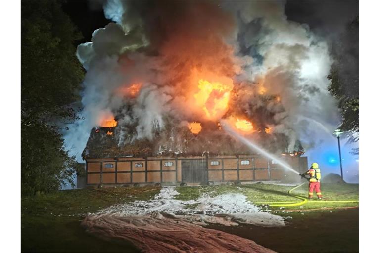 Feuerwehrleute löschen das Feuer in der mit Reet gedeckten Museumsscheune. Foto: -/TNN/dpa