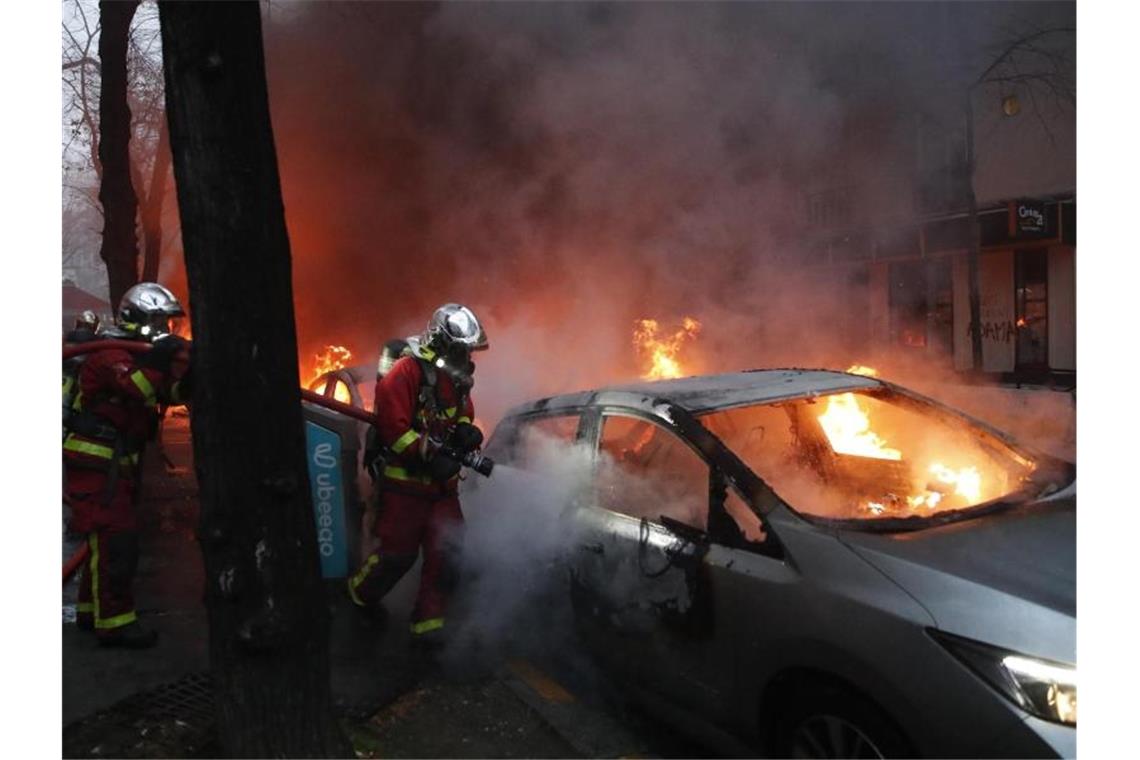 Feuerwehrleute löschen während eines Protestes auf einer Straße ein brennendes Auto. Foto: Francois Mori/AP/dpa