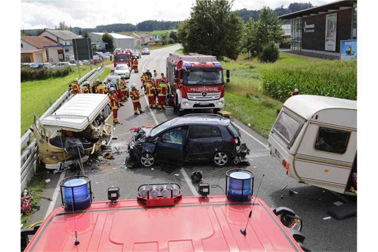 Feuerwehrleute stehen an der Unfallstelle mit einem Kleinbus und einem Wohnwagengespann. Foto: Ralf Zwiebler