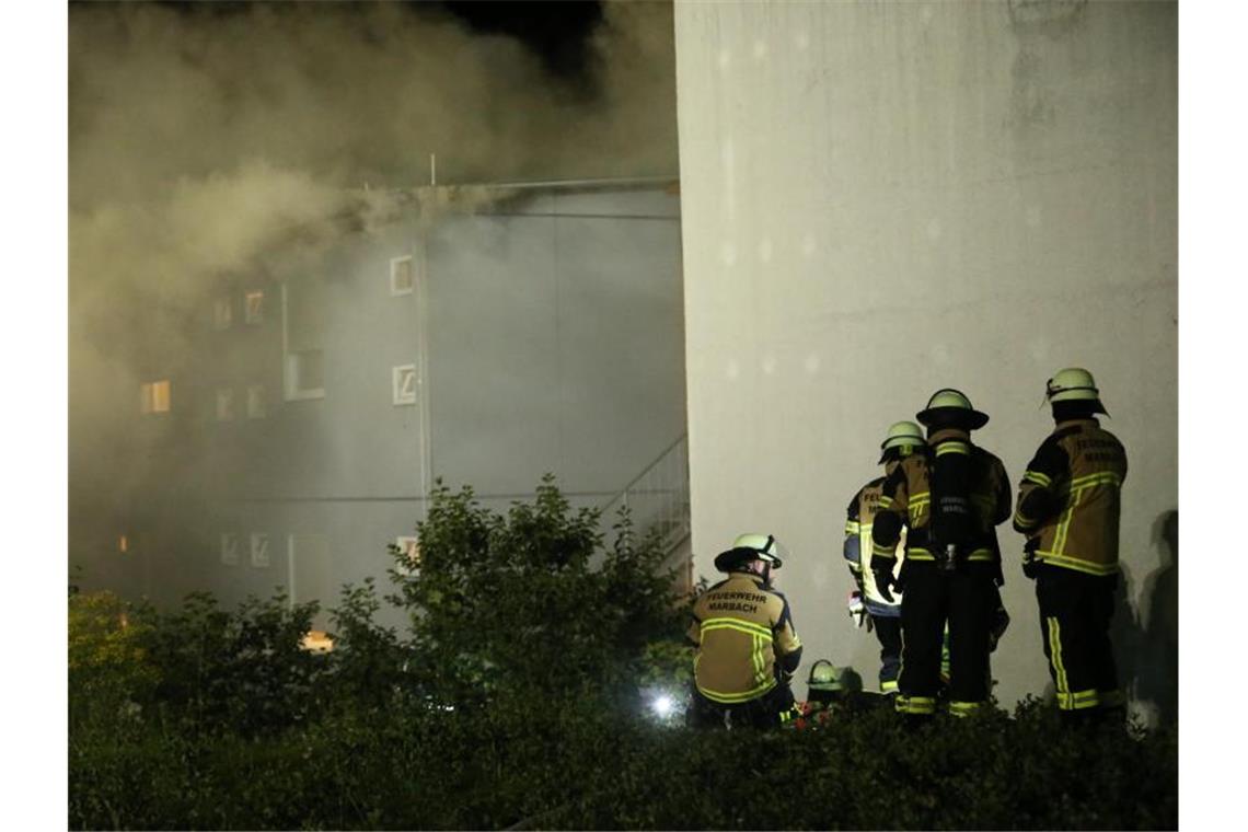 Feuerwehrleute stehen an einer Container-Unterkunft für Asylbewerber, aus der dichter Rauch quillt. Foto: Karsten Schmalz