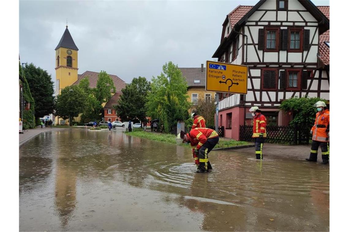 Unwetter erwartet - Überschwemmung in Karlsbad Feuerwehrleute stehen nach einem Unwetter auf einer überfluteten Straße. Foto: Thomas Riedel/dpa