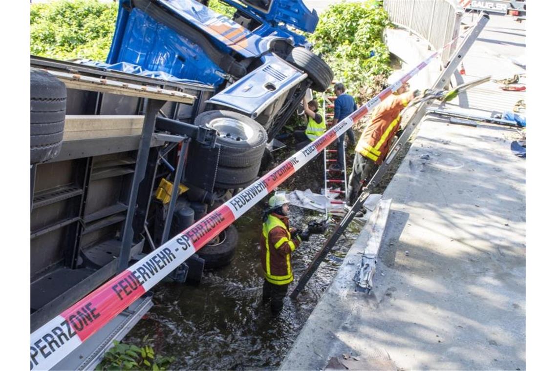 Sattelzug durchbricht Brückengeländer und landet im Fluss Feuerwehrleute stehen neben einem Lastwagen, der in einen Fluss gekippt ist. Foto: Stefan Puchner/dpa