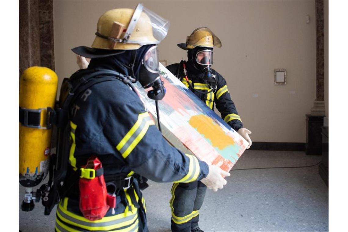 Feuerwehrleute tragen ein Kunstwerk aus der Staatsgalerie. Foto: Tom Weller/dpa