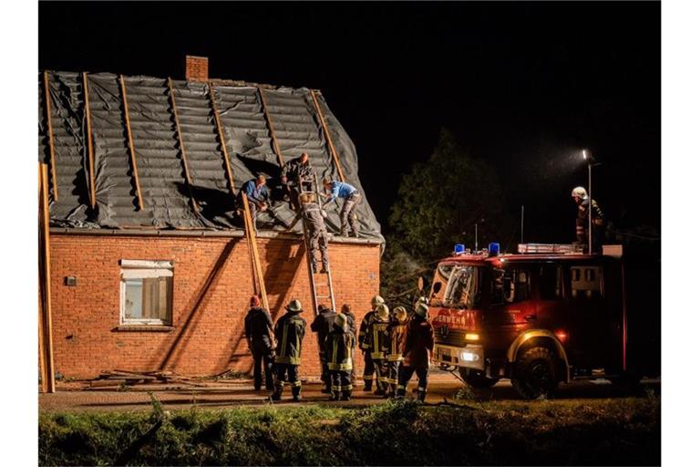 Feuerwehrleute und Helfer reparieren das Dach eines beschädigten Hauses in Berumerfehn. Foto: Mohssen Assanimoghaddam/dpa