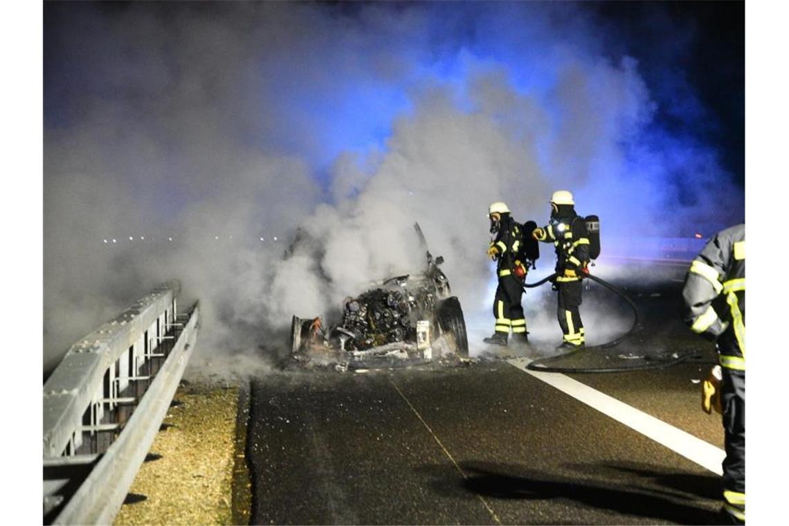 Feuerwehrleute versuchen am Samstagabend ein brennendes Fahrzeug auf der A6 zu löschen. Foto: Priebe/dpa