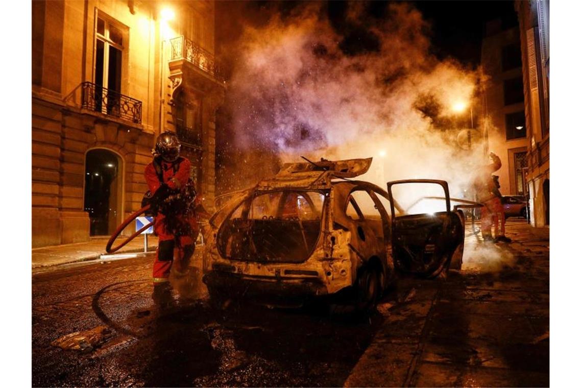 Feuerwehrmänner löschen ein brennendes Auto in der Nähe der Champs-Elysées. Foto: Sameer Al-Doumy/AFP/dpa