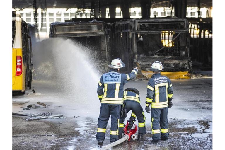 Feuerwehrmänner stehen bei Nachlöscharbeiten vor ausgebrannte Bussen. Foto: Tom Weller/dpa/Archivbild