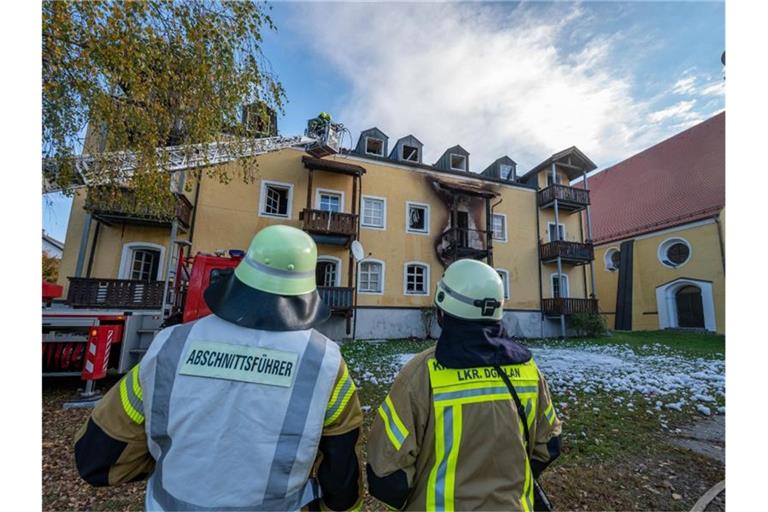 Feuerwehrmänner stehen vor einem ausgebrannten Mehrfamilienhaus. Foto: Armin Weigel/dpa