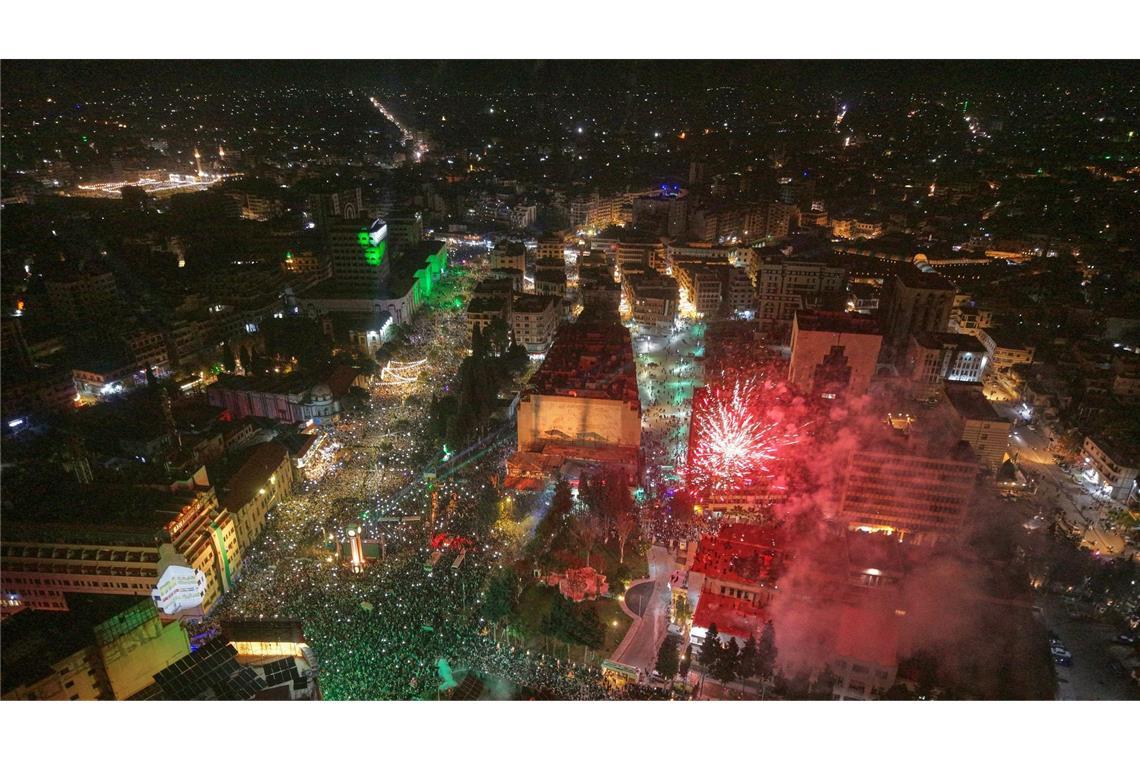 Feuerwerk erhellt den Himmel, während die Menschen den Clock Square in der syischen Stadt Homs anlässlich des ersten Jahrestags des Sturzes des Regimes von Bashar Assad füllen.