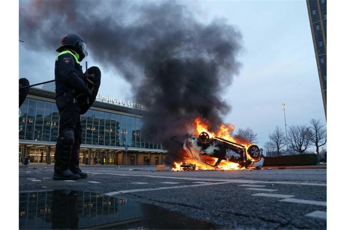 Niederlande: Krawalle bei Protesten gegen Corona-Maßnahmen Flammen schlagen aus einem Auto, das vor dem Bahnhof in Eindhoven auf dem Kopf liegt. Foto: Rob Engelaar/ANP/dpa