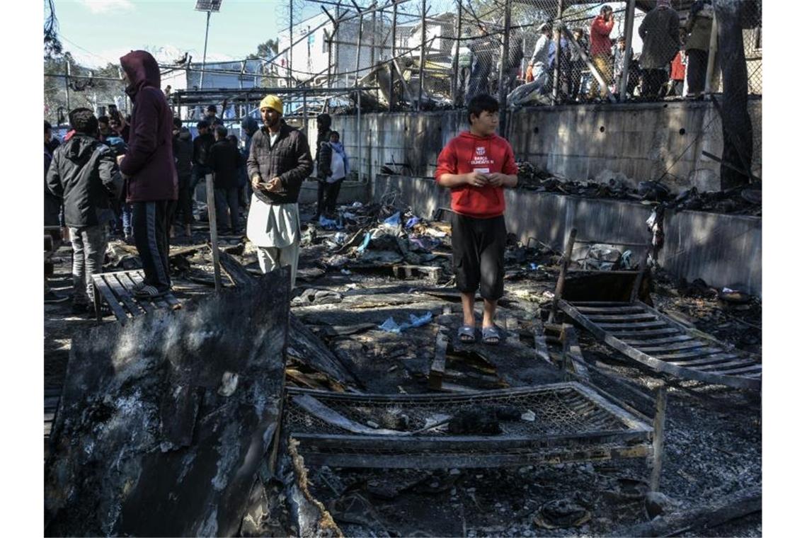 Flüchtlinge stehen im Lager Moria auf den abgebrannten Überresten eines Containerhauses. Foto: Panagiotis Balaskas/AP/dpa