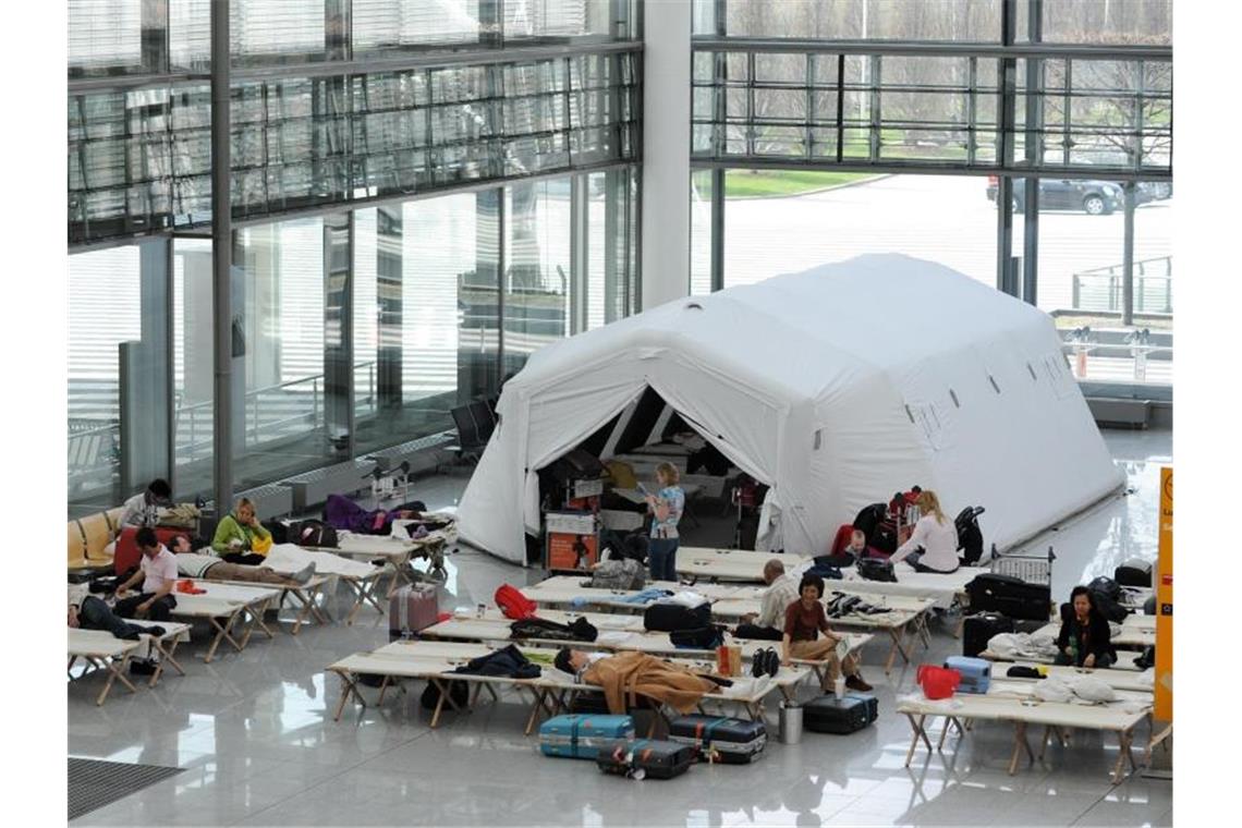 Fluggäste sitzen am Münchener Flughafen auf Feldbetten in einer Notunterkunft im Terminal 2. Foto: Tobias Hase/dpa