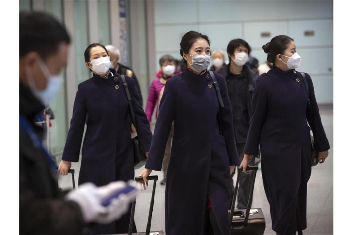 Flughafenpersonal und Mitglieder von Flugzeugbesatzungen tragen am Flughafen von Peking Atemschutzmasken. Foto: Mark Schiefelbein/AP/dpa