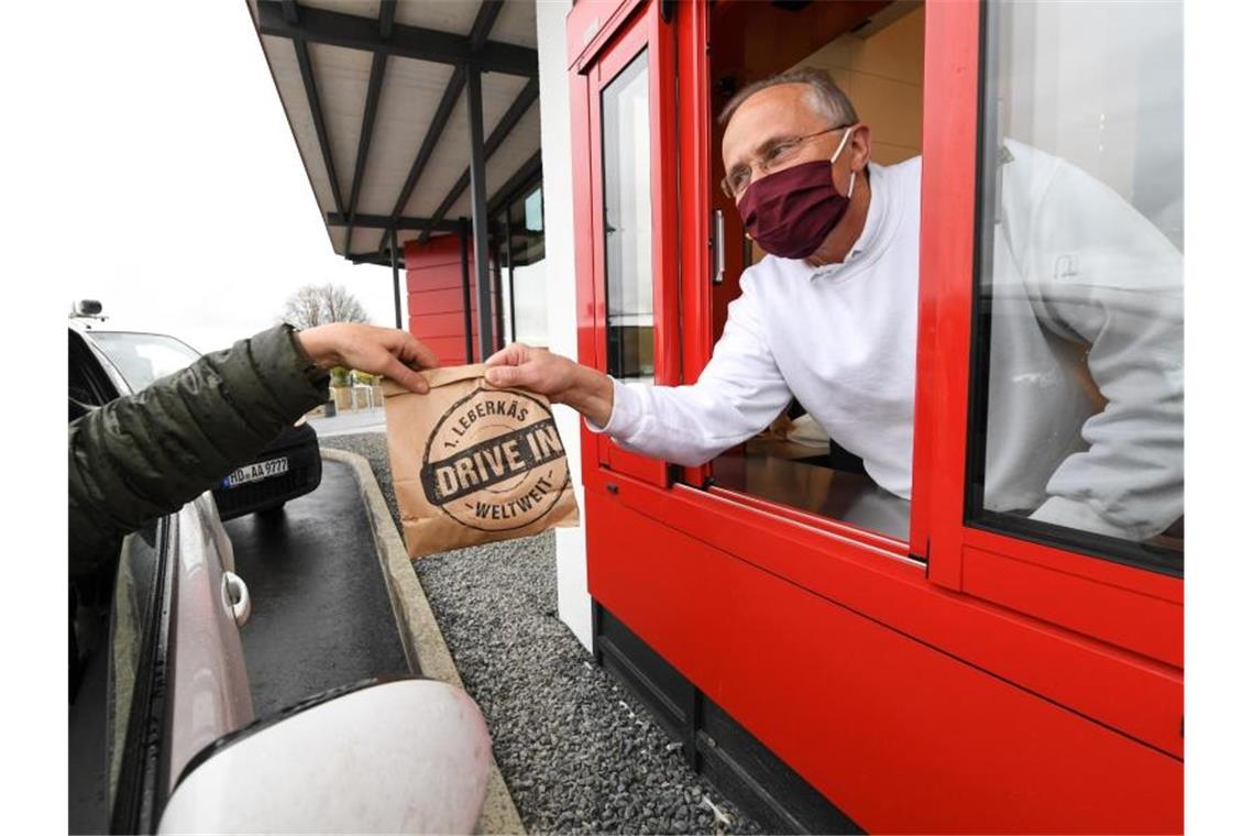 Franz Weinbuch (r) von der Metzergei Weinbuch reicht einem Kunden am Läberkäs-Drive-in-Schalter seine Bestellung ins Auto. Foto: Felix Kästle/dpa/Archivbild