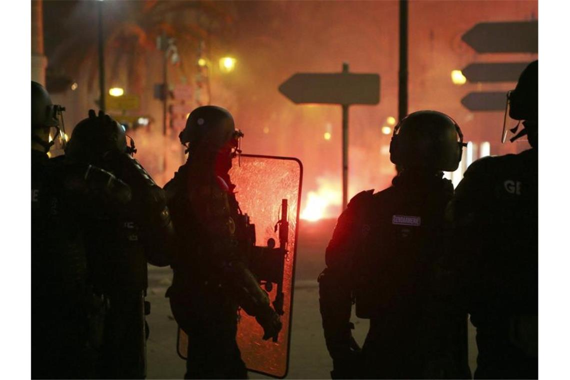 Rückkehr korsischer Nationalisten auf Insel möglich Französische Gendarmen stehen auf der Straße in Ajaccio auf Korsika, während es im Hintergrund brennt. Foto: Pascal Pochard-Casabianca/AFP/dpa
