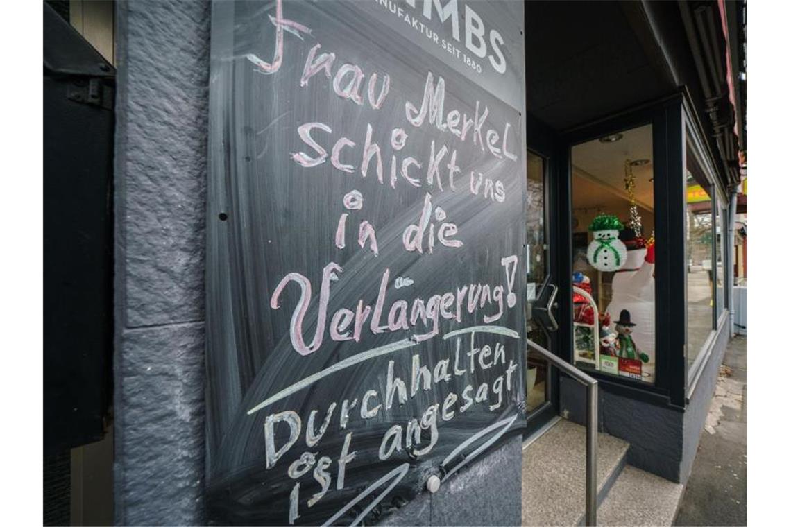 „Frau Merkel schickt uns in die Verlängerung! Durchhalten ist angesagt!“ steht auf einer Tafel neben einem geschlossenen Geschäft im hessischen Friedberg. Foto: Frank Rumpenhorst/dpa