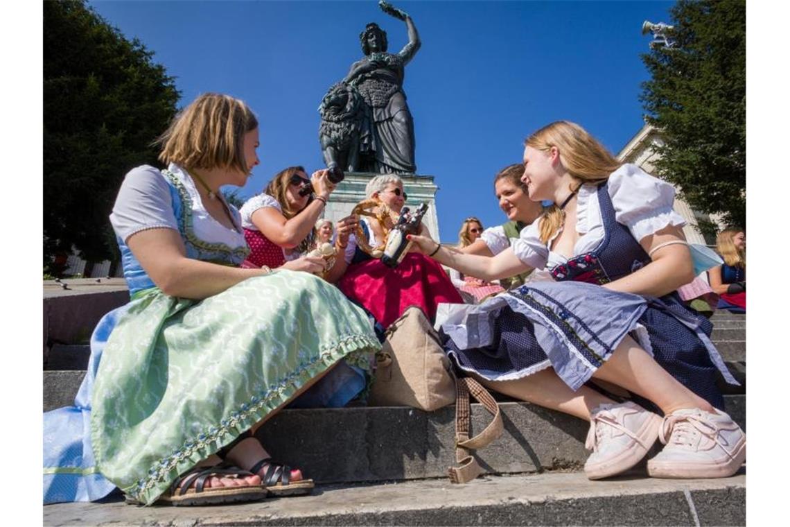 Frauen in Tracht sitzen auf dem Wiesn-Gelände auf der Freitreppe unterhalb der Bavaria-Statue. Foto: Peter Kneffel/dpa