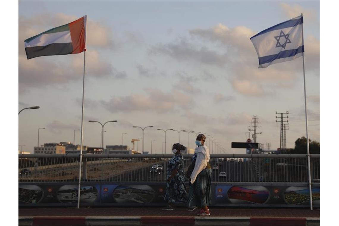 Präsident der Emirate hebt Boykott Israels per Dekret auf Frauen mit Schutzmasken gehen an den Flaggen von Israel und den Vereinigten Arabischen Emiraten auf der Friedensbrücke im israelischen Netanya vorbei. Foto: Ariel Schalit/AP/dpa