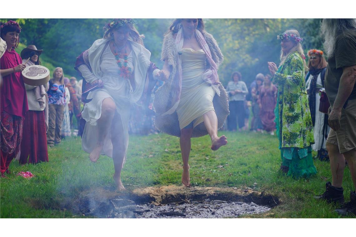 Frauen springen beim Beltane-Festival am Glastonbury Chalice Well in England über das Feuer.