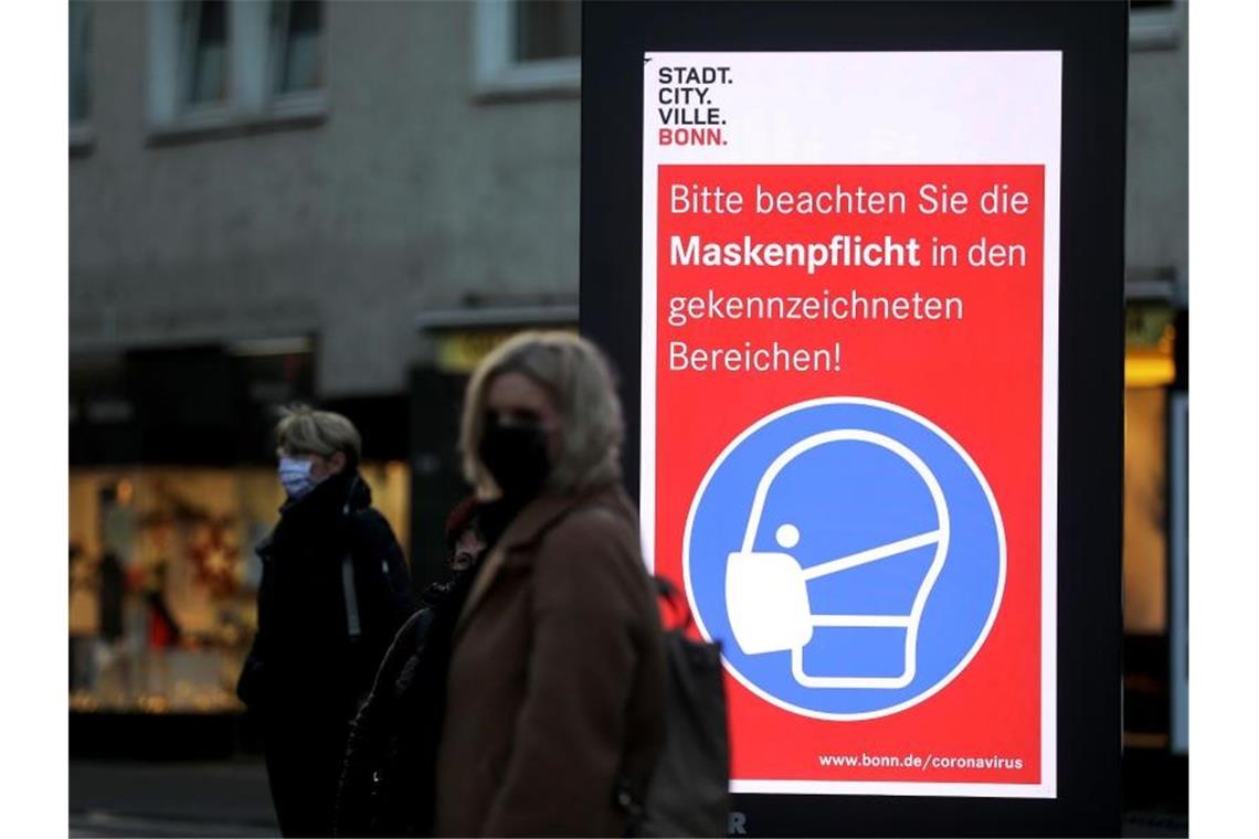 Frauen stehen neben einem Hinweisschild zur Maskenpflicht an einer Haltestelle in Bonn. Die Länder fordern vor den Beratungen mit Kanzlerin Merkel strengere Kontaktbeschränkungen, um die hohen Coronazahlen zu senken. Foto: Oliver Berg/dpa