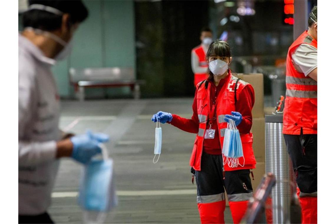 Freiwillige Mitarbeiter des Roten Kreuzes verteilen vor dem Bahnhof Barcelona-Catalunya Mundschutzmasken an Passagiere. Foto: Jordi Boixareu/ZUMA Wire/dpa