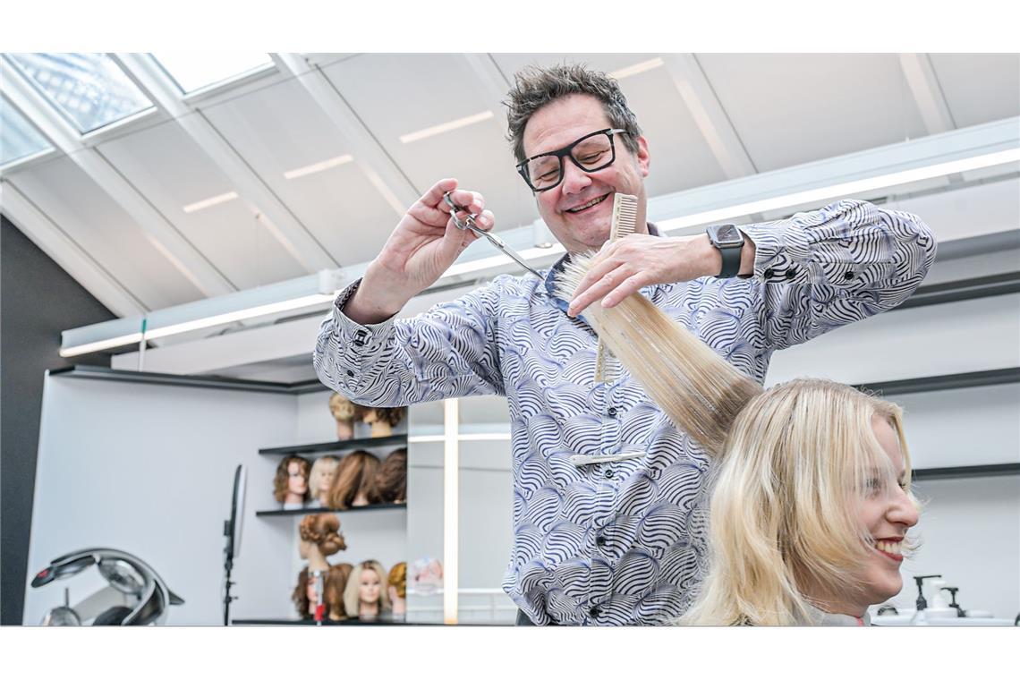 Friseur Holger Schier steht in seinem Friseursalon in Heidenheim an der Brenz und schneidet einer Kundin die Haare.
