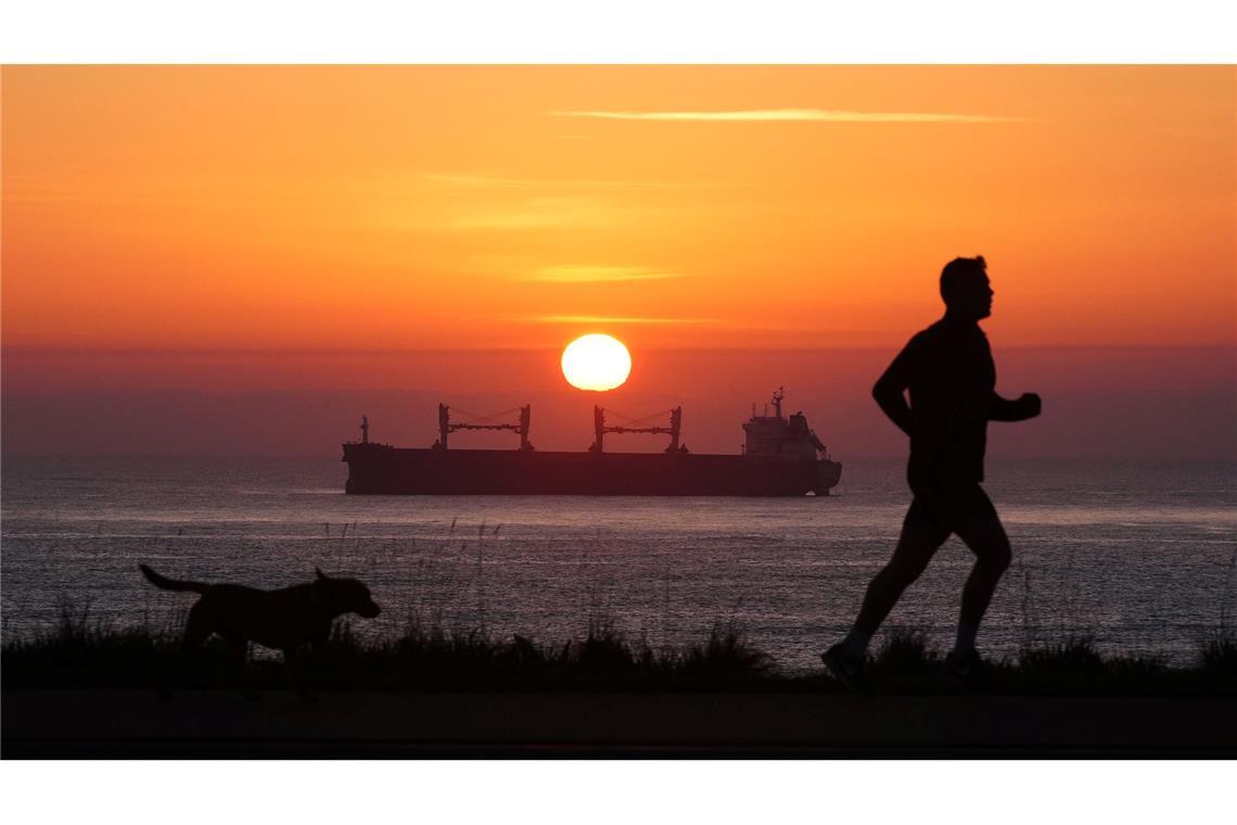Bilder des Tages Früh unterwegs: Ein Mann joggt am Morgen an der Nordostküste von Großbritannien, während die Sonne am Horizont über einem Frachter aufgeht.
